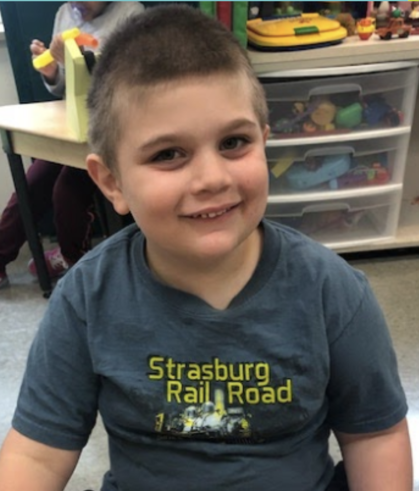 Young boy smiling wearing a gray shirt in school