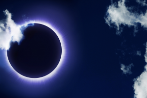 an eclipse; the sun covered by the dark moon in a dark blue sky with white clouds