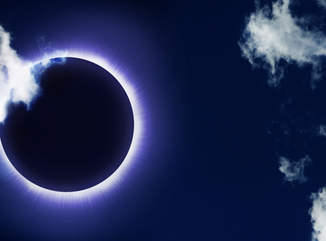 an eclipse; the sun covered by the dark moon in a dark blue sky with white clouds