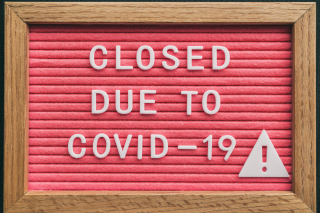 brown and red wooden sign that reads "CLOSED DUE TO COVID-19" with a caution sign in white letters