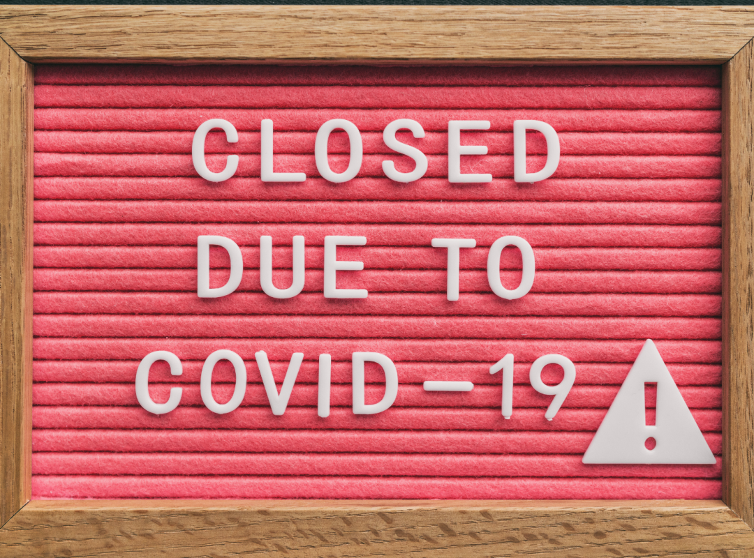 brown and red wooden sign that reads "CLOSED DUE TO COVID-19" with a caution sign in white letters
