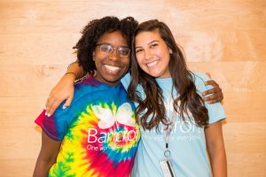 Two female direct support professionals, hugging and smiling at the camera.