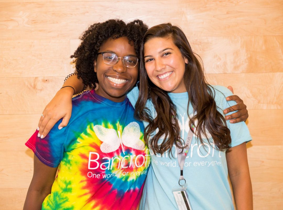 Two female direct support professionals, hugging and smiling at the camera.