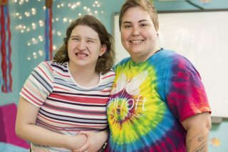 Bancroft Direct Support Professional standing with girl in a teal blue room.