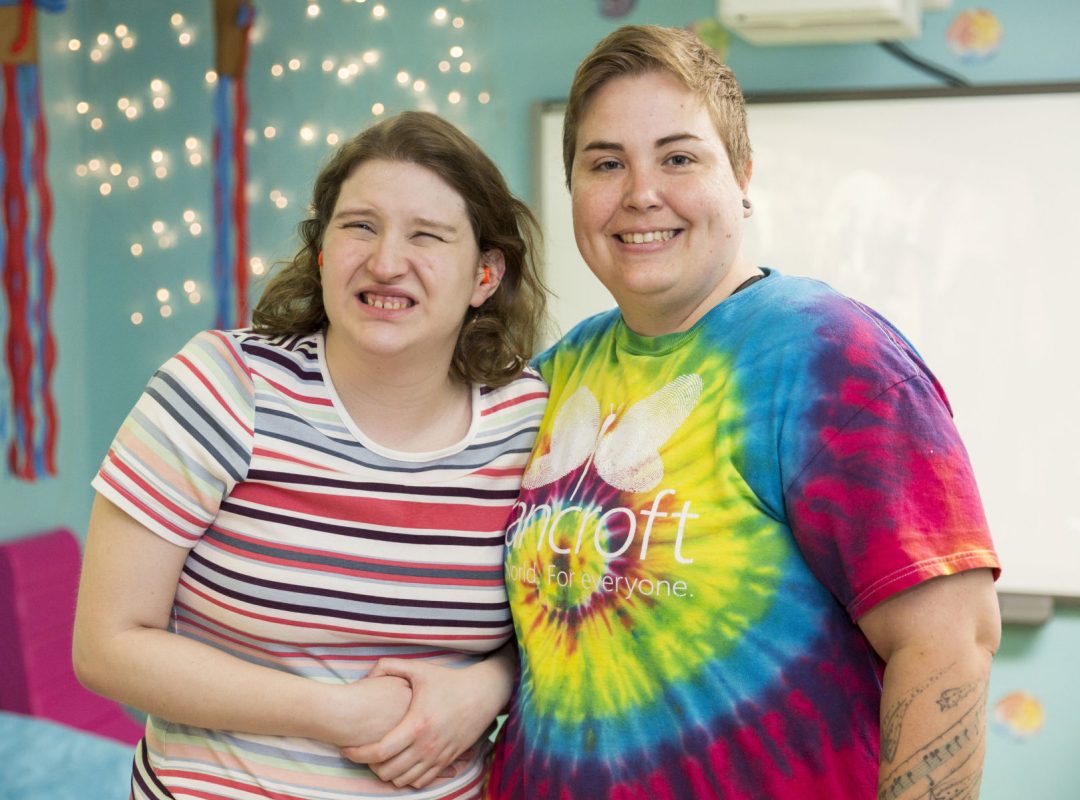 Community_Residential_DE-2 Bancroft Direct Support Professional standing with girl in a teal blue room.