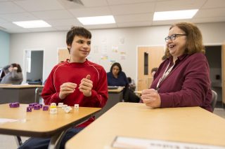 Paraprofessional sitting at desk laughing with student.