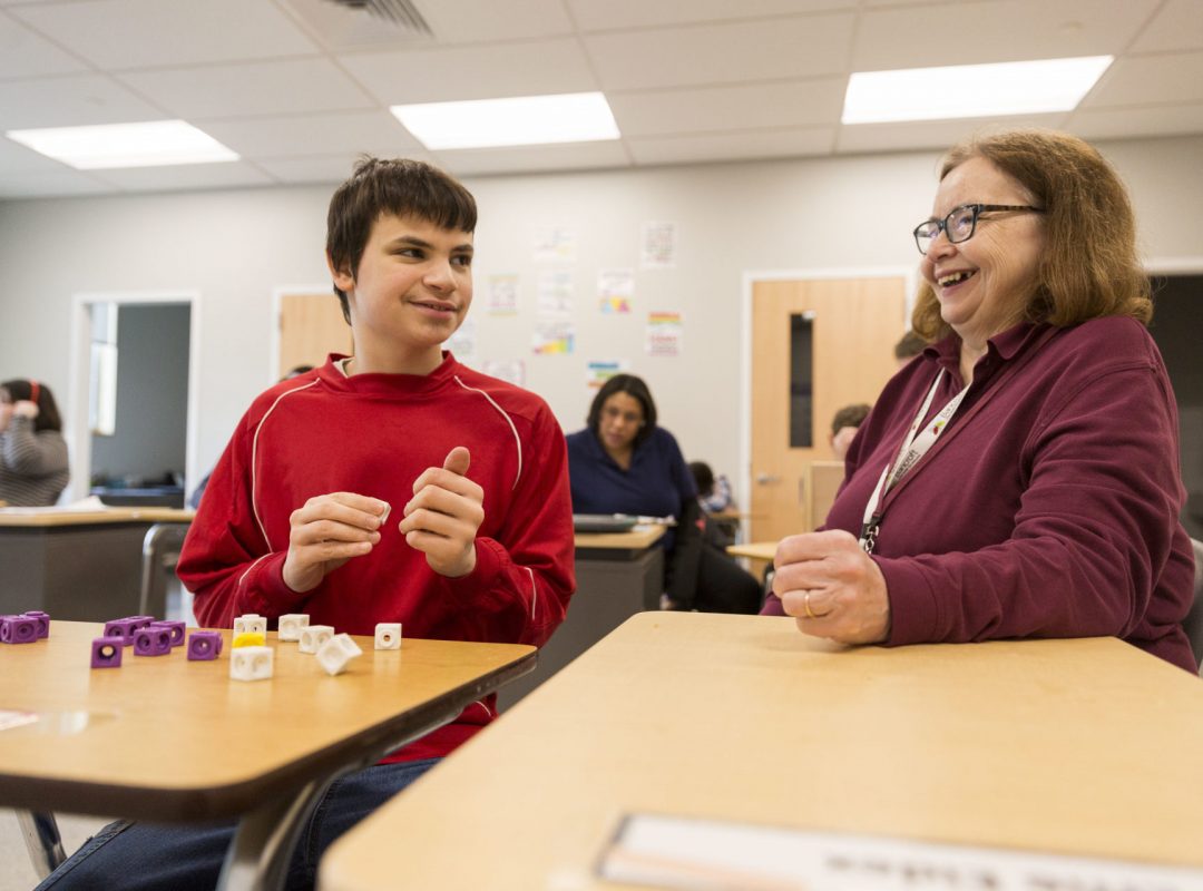 Paraprofessional sitting at desk laughing with student.