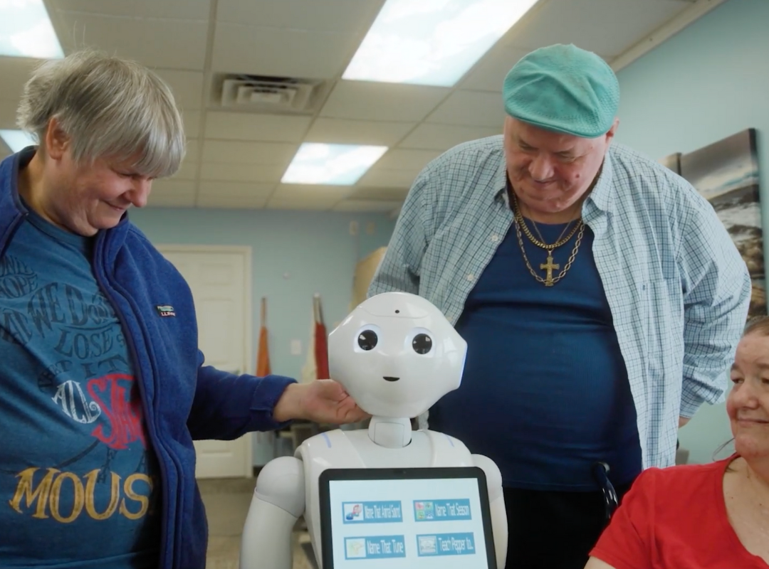 group of residents of Bancroft's Flicker residential program for older adults with autism and other I/DD stand with Pepper, the humanoid AI robot