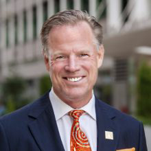 Light-skinned man in a blue suite and orange tie with circles on it
