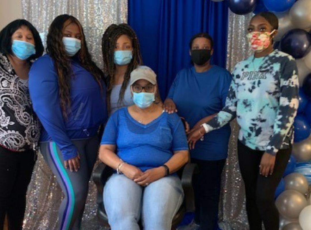six women in blue shirts stand in front of a silver and blue sparkly background smiling