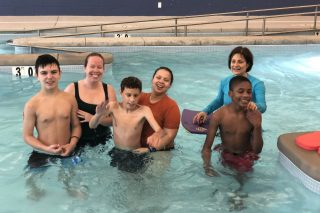 six paraprofessionals and students stand in a swimming pool smiling