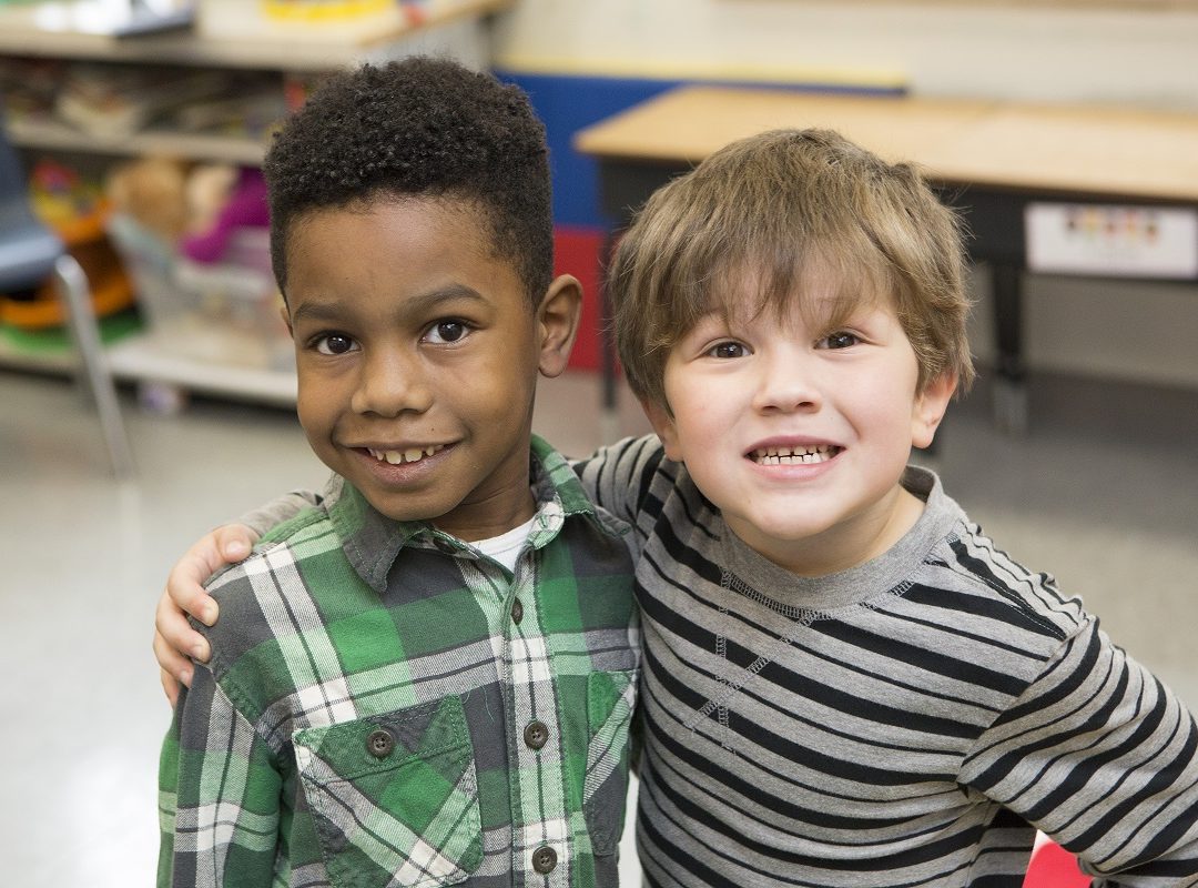 a young boy in a green plaid shirt and a young bow in a gray and black striped shirt stand together and smile
