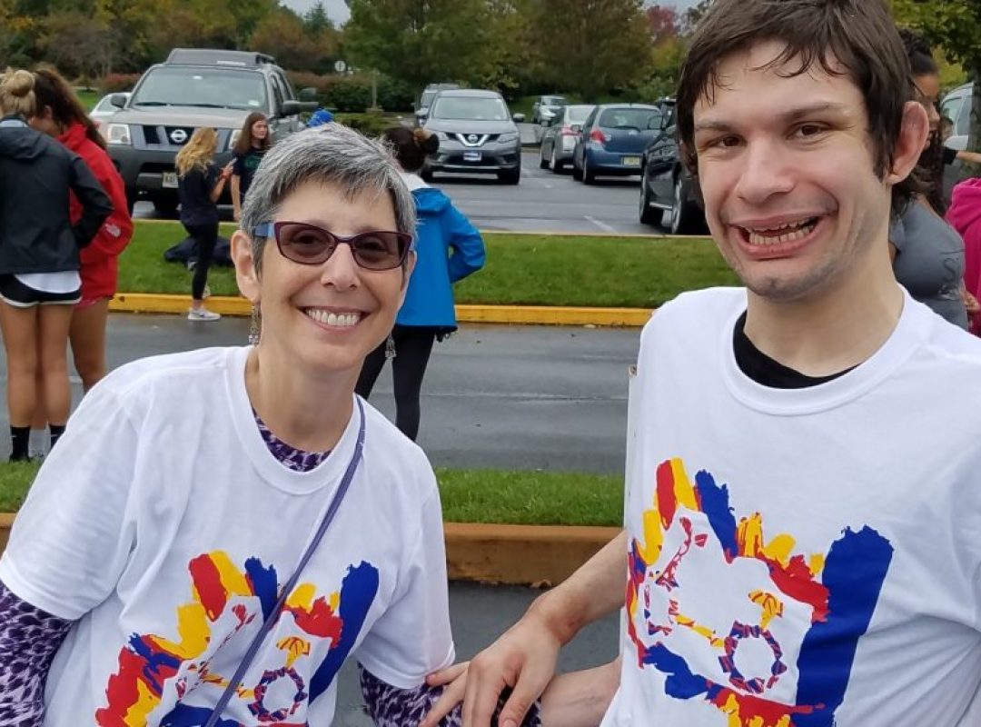 A mother and her adult son are wearing matching white t-shirts and are smiling at the camera. Her son is a resident in a Bancroft adult group home.