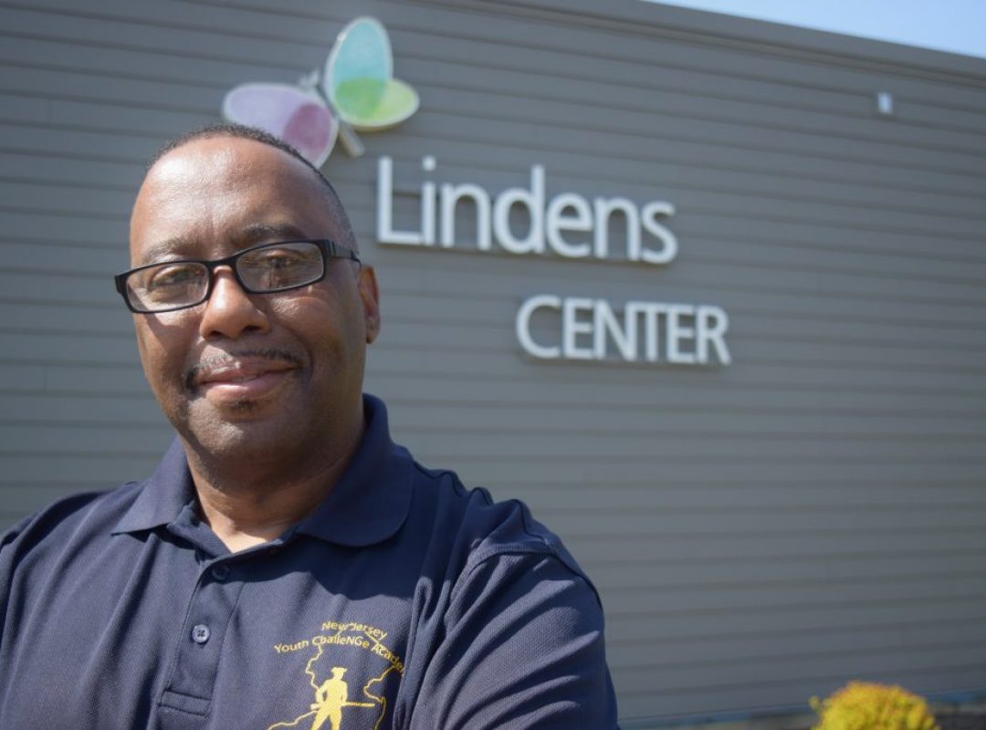 Michael Bradley, a man with glasses, short black head and facial hair in a blue polo stands in front of the Linden's Center building