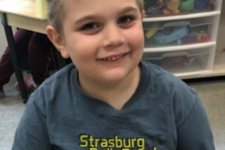 Young boy smiling wearing a gray shirt in school