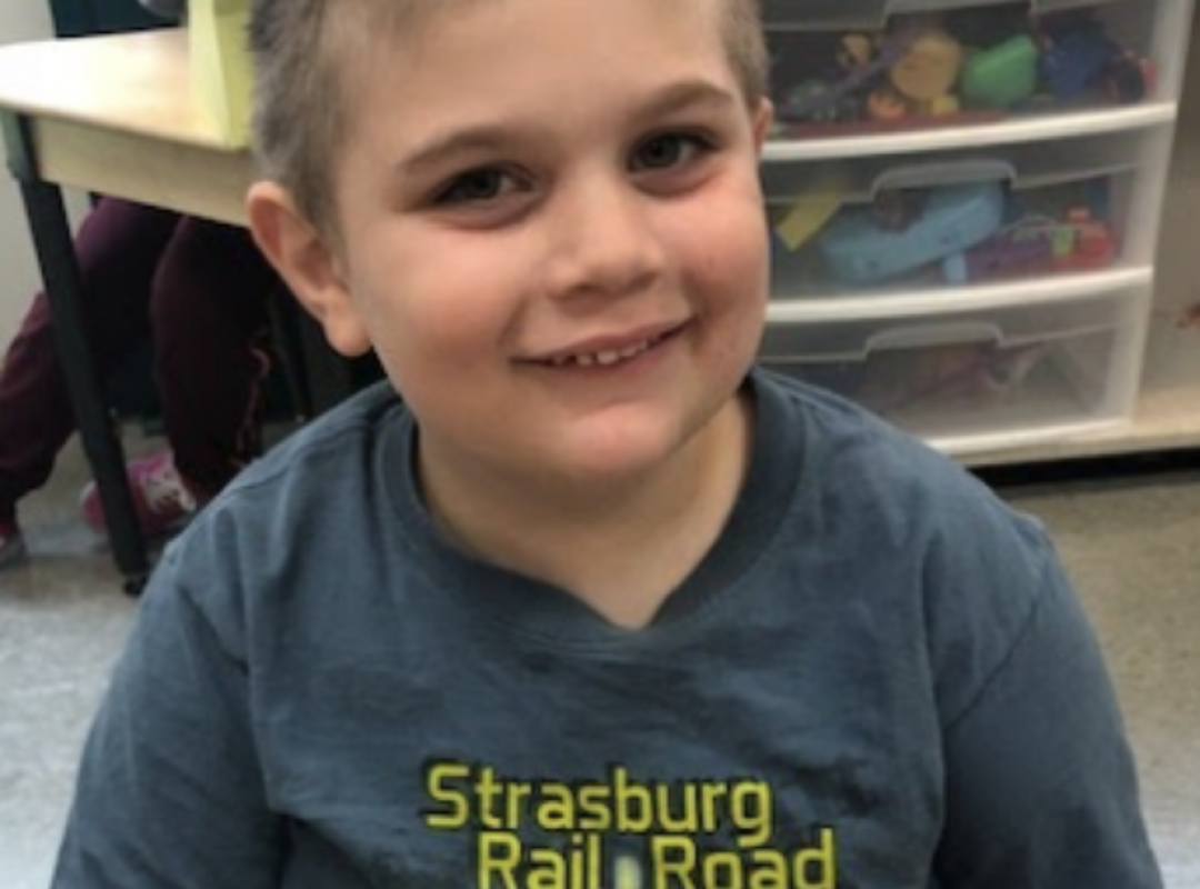 Young boy smiling wearing a gray shirt in school