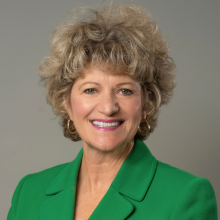 Light-skinned woman in green suit with blonde hair smiles