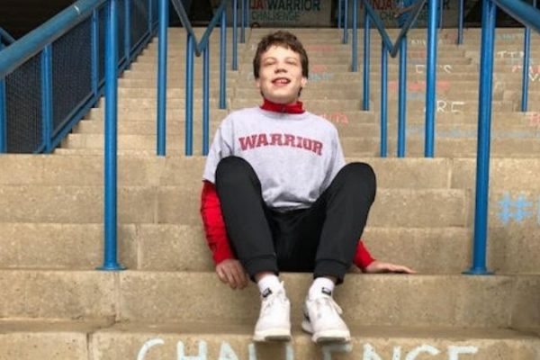 Young boy with brown hair sitting on steps outside.