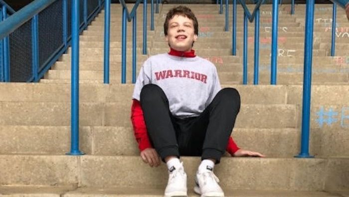 Young boy with brown hair sitting on steps outside.