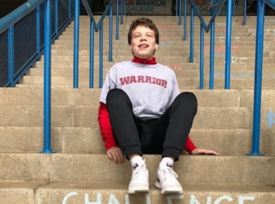 Young boy with brown hair sitting on steps outside.