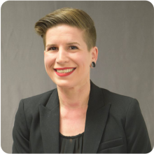 Kellie Goldberg, a light-skinned blonde woman with short blonde hair and wearing a black suit, smiles