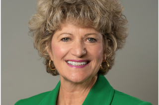 Toni Pergolin's headshot where she is smiling and wearing a green blazer jacket