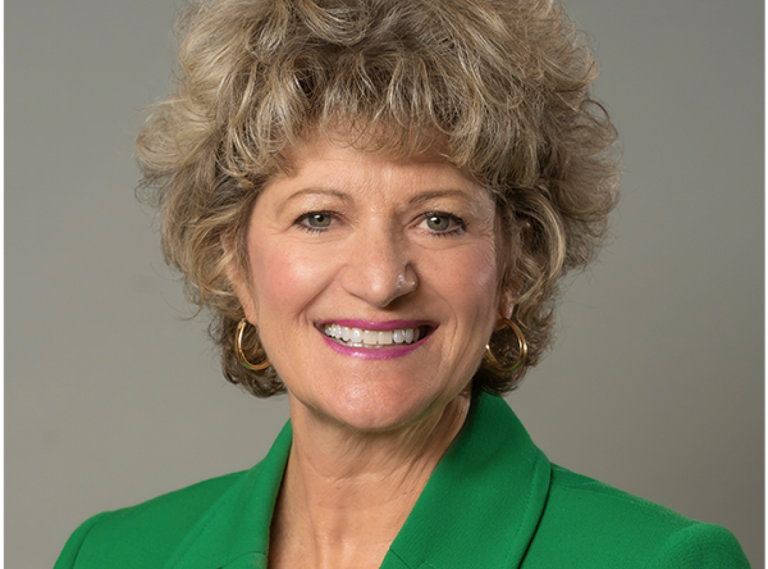 Toni Pergolin's headshot where she is smiling and wearing a green blazer jacket