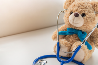 a brown teddy bear with a blue bow sits on a table wearing a stethoscope