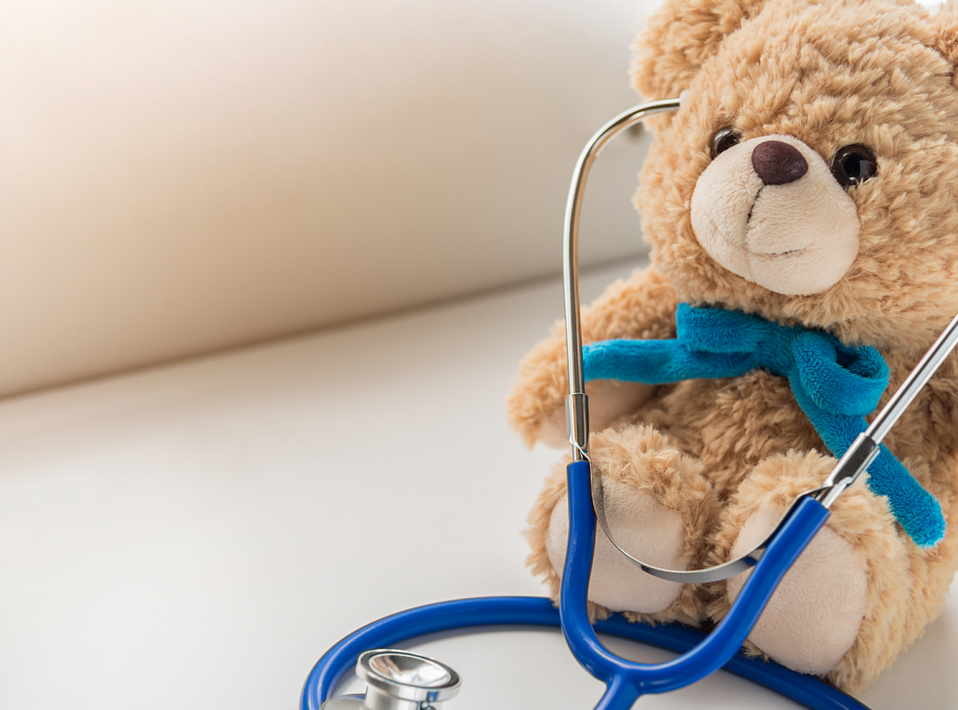 a brown teddy bear with a blue bow sits on a table wearing a stethoscope