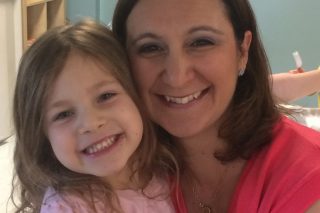 a woman and her daughter both dressed in pink tops with brown hair hold each other and smile