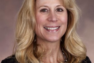 Susan Piergallini, a light-skinned woman with blonde hair wearing a black blouse, smiles