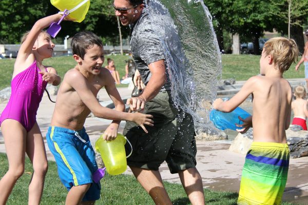 three children and a man in swimsuits use buckets to splash water on each other