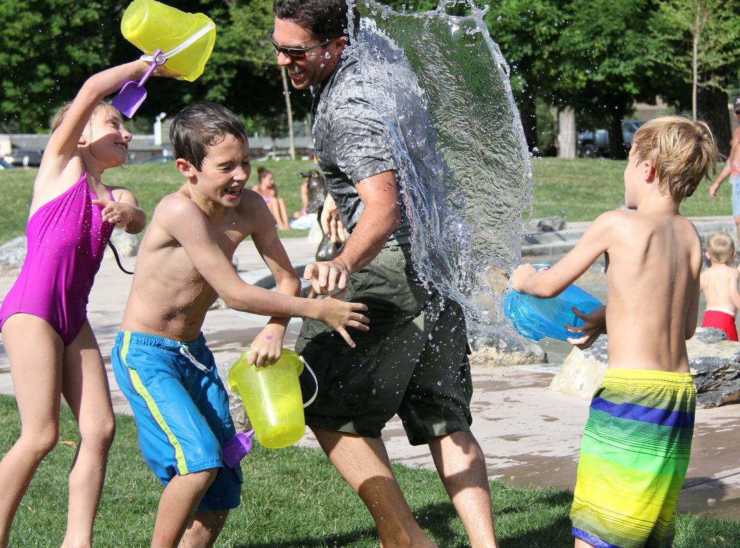 three children and a man in swimsuits use buckets to splash water on each other